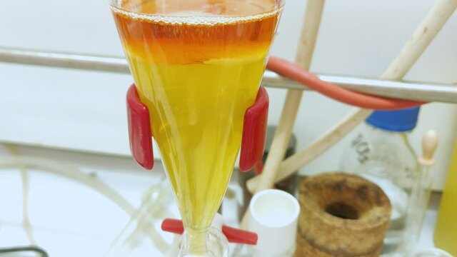 Separation of organic layer and water layer in separating funnel in a chemistry lab for education purpose. Effervescent of carbon dioxide bubble in organic layer. 4K scientific background concept.