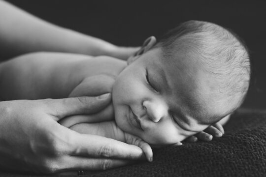 Female hands hug sleeping naked newborn. Black and white photo