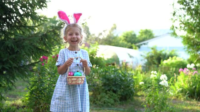 a little blonde girl with bunny ears holding a basket of painted Easter eggs in her hands and laughing, the concept of a religious holiday