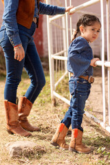Child and unrecognizable woman in cowgirl clothes in a ranch