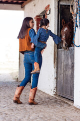Mother and daughter cowgirls interacting with a horse in a barn