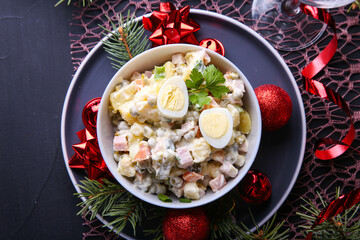 Traditional Russian salad Olivier for Christmas and New Year on a dark background. Fir tree branches, red ribbons and balls. Close up view