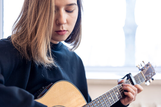 Serious young woman playing acoustic guitar at home.