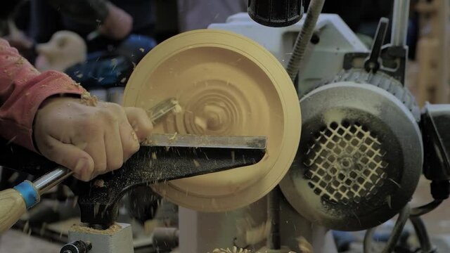 Man carpenter holding gouge for shaping piece of wood on turning lathe machine with many shavings at workshop - close up, slow motion. Carpentry, hobby, craftsmanship and manufacturing concept