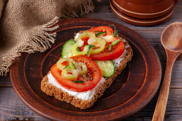 sandwich with cheese, tomato, cucumber and pepper on a brown clay plate