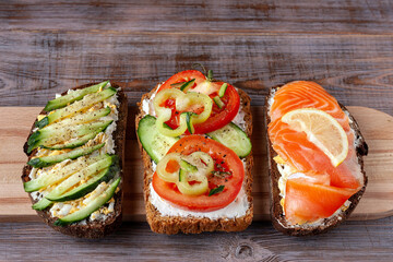 sandwiches with salmon, tomatoes, cucumbers, egg and cheese on a wooden board