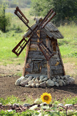 Wooden old windmill in sunflowers and stones on a country plot. A real high windmill with spinning blades. Rustic theme as a decoration.