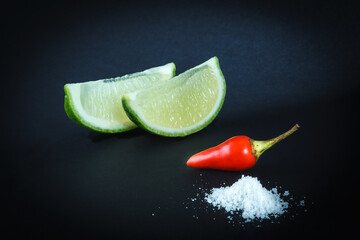 Red chili peppers, lime and salt on black background
