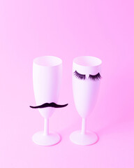 Two white champagne glasses. One with eyelashes, the other with a mustache. Pink background Party celebration futuristic surreal aesthetic concept