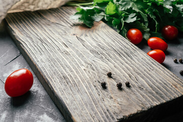 Textured cutting board on gray concrete surface with cherry tomatoes, parsley and peppercorns. Cooking food concept. Copy space