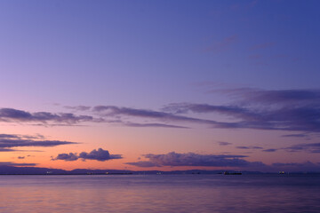 Fototapeta na wymiar 兵庫県芦屋市芦屋浜の夜明け。日の出とともに あたりはオレンジ色に染まる。大阪湾を隔てて大阪府の市街地と和泉山地がシルエットで浮かぶ