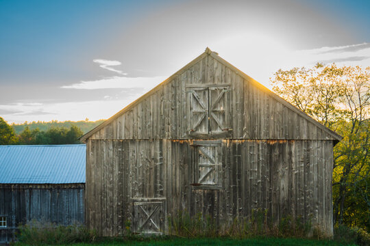 rustic gray barn back lit by the setting sun on a country road 
