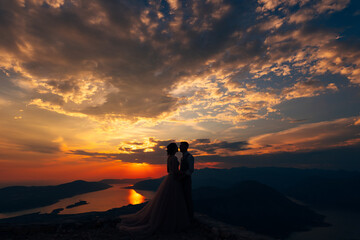 Groom and bride stand on the mountain against the background of sunset