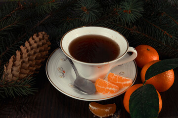 Mug of tea with tangerines and Christmas tree branches. Dark background.