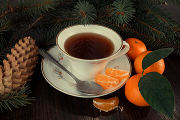 Mug of tea with tangerines and Christmas tree branches. Dark background.