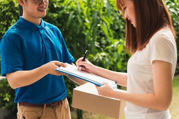 Asian beautiful customer young woman signing delivery in clipboard get her package from service courier man, smiling female signature receipt of delivery package at door front house