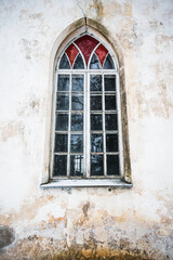 Large window with stained glass and old, peeled wall. Old historical lutheran church, Barbele, Latvia