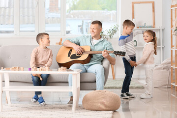 Father playing guitar and little children spending time together at home
