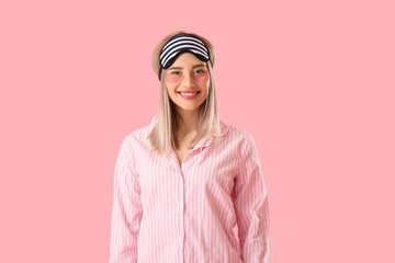 Pretty young woman with sleeping mask and under-eye patches on pink background