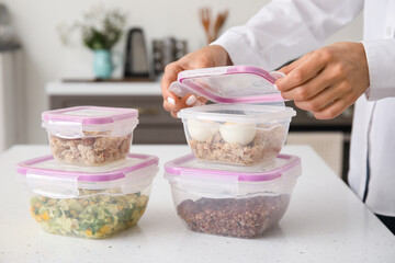 Woman packing delicious healthy meal into containers on table in kitchen