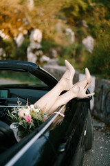 Bride legs in high-heeled shoes on the convertible door. Close-up