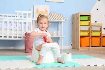 Cute baby girl sitting on potty at home