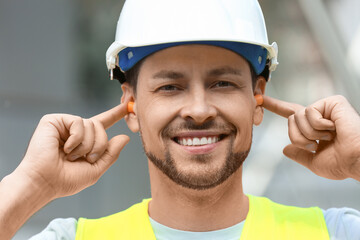 Male worker putting ear plugs outdoors, closeup