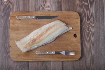 cod filet with knife and fork on the wooden table