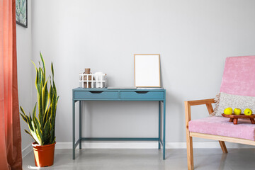 Blue table with blank frame, basket, vases and laptop near light wall in room