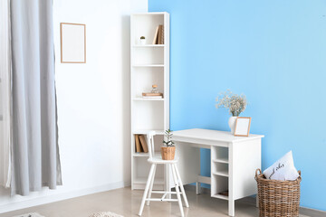 Interior of light room with modern workplace, shelving unit and blue wall