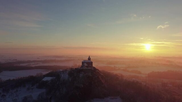 Aerial, early morning view of the Castle standing on the hill above fog at sunrise, light by morning sun rays.