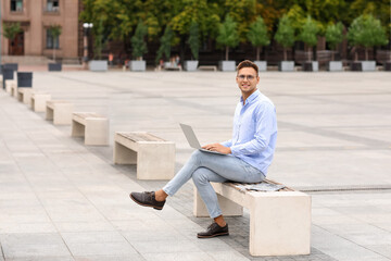 Handsome young businessman using laptop on city square