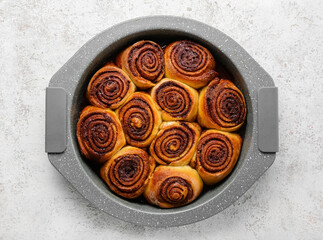 Baking dish with tasty cinnamon rolls on light background