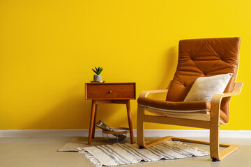 Stylish interior with bedside table and armchair on yellow wall background