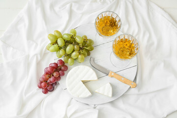 Wooden board with ripe grapes, cheese and glasses of wine on light background