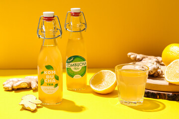 Glass and bottles of fresh kombucha on color background