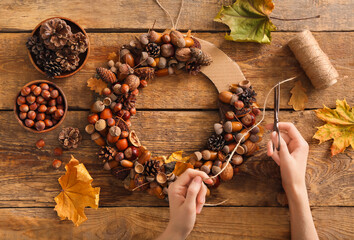 Woman making beautiful acorn wreath on wooden background