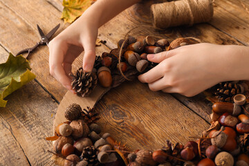 Woman making beautiful acorn wreath on wooden background, closeup © Pixel-Shot
