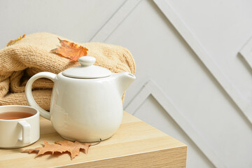 Tea pot, cup of hot beverage and autumn leaves on table near grey wall