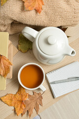 Tea pot, cup of hot beverage and autumn leaves on wooden background