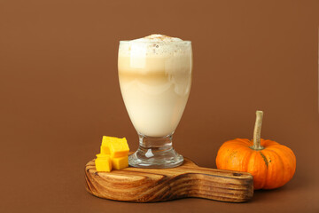 Glass of tasty pumpkin latte on brown background