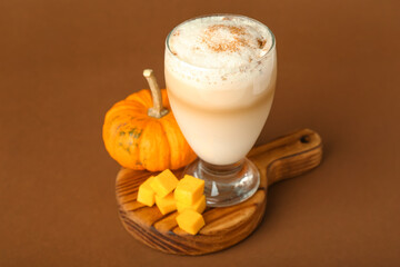 Glass of tasty pumpkin latte on brown background