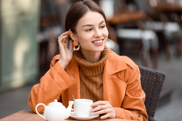 Smiling woman with cup of tea enjoying autumn day in street cafe