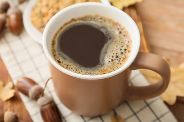 Cup of coffee with acorns on table, closeup