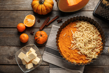 Baking dish with uncooked pumpkin pie and ingredients on wooden background