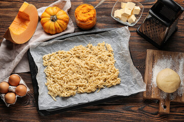 Baking dish with grated dough for pumpkin pie and ingredients on wooden background