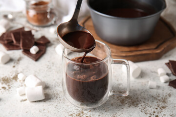 Pouring of tasty hot chocolate into glass cup on light background