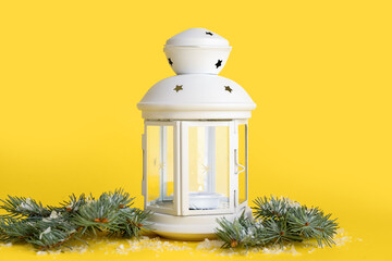 Beautiful Christmas lantern with burning candle and fir branches on yellow background