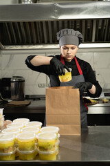 Young caucasian woman wearing an apron and gloves puts disposable plastic food containers in a...