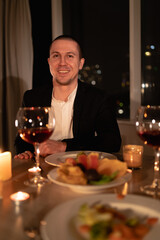 valentine's day dinner, portrait of a man at a festive table with red wine and candles, romantic home date, the guy prepared a surprise for girlfriend